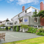 Incorporating Wellness Into Your Home’s Exterior Design A modernly built house with a tennis court in the backyard. The backyard is beautifully landscaped with trees and plants.