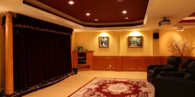 Three leather recliners sit on a red oriental rug in a home theater with recessed lighting and a velvet curtain.