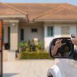 A person driving a silver car pushes the button on a remote that opens an automatic gate for their home's driveway.