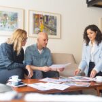 Various Ways Designers Utilize Metal Mesh Two women and a man sit on a couch and chairs, looking at papers that sit on a wooden coffee table.