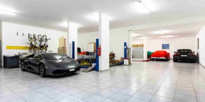 Three cars parked in a tiled garage with white walls, a four-post auto lift, hanging bikes, and storage cabinets.