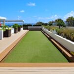Why You Should Hire Professional Artificial Turf Installers A modern rooftop terrace with multiple shaded seating areas, long planters, and a strip of artificial turf in the middle.