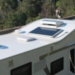 Top Accessories for a More Functional RV Roof An overhead view of an RV parked on a roadway in full sun. The RV's roof has a solar panel and the RV roof vents are open.