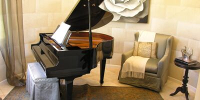 A grand piano sits in a rounded part of a room with other furniture and accessories, including a rose painting behind it.
