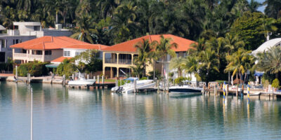 A neighborhood of luxury waterfront homes with palm trees in the homes' backyards, and boat docks in their front yards.