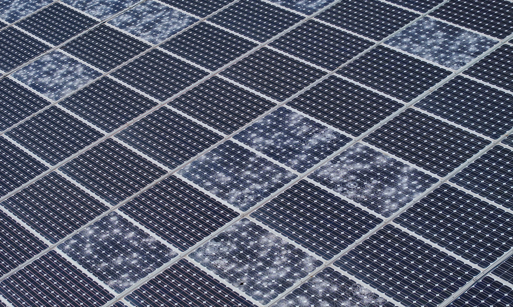 An aerial view of a large solar panel. Several individual cells on the panel are cracked from hail damage.