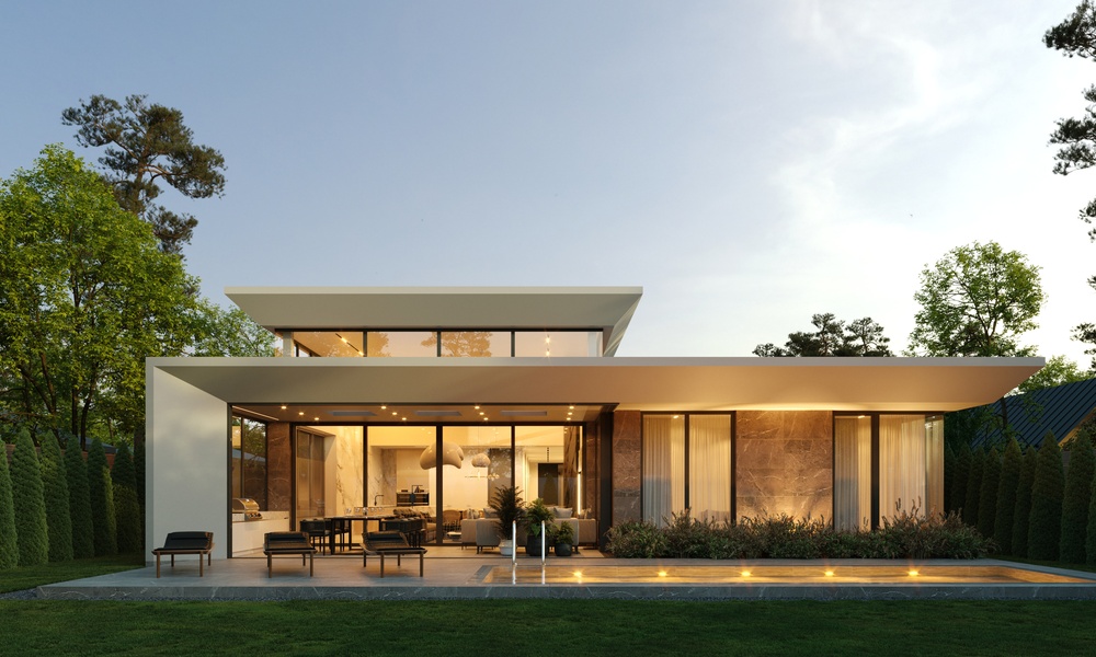 A long shot of a luxurious flat-roofed home with warm lighting illuminating its exterior walls and landscaping.