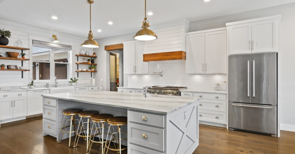 A wide view of a modern farmhouse kitchen, including white cabinetry, a large white counter island, and open shelving.